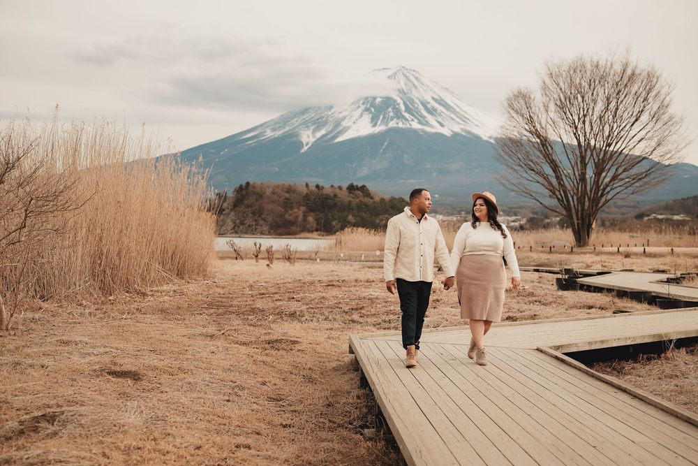 People walking on wooden boardwalk against majestic mountain backdrop with Mt Fuji in view on winter day.