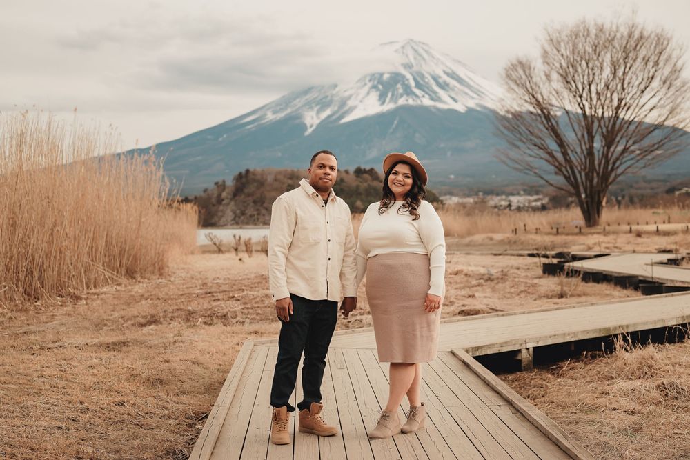 A couple shares an intimate moment on a wooden boardwalk with Mount Fuji visible in the background on a winter day.