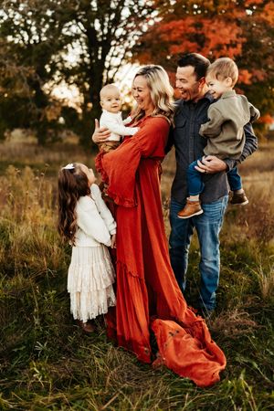 A family shares joyful moments together in a field during autumn with vibrant orange foliage in the background.