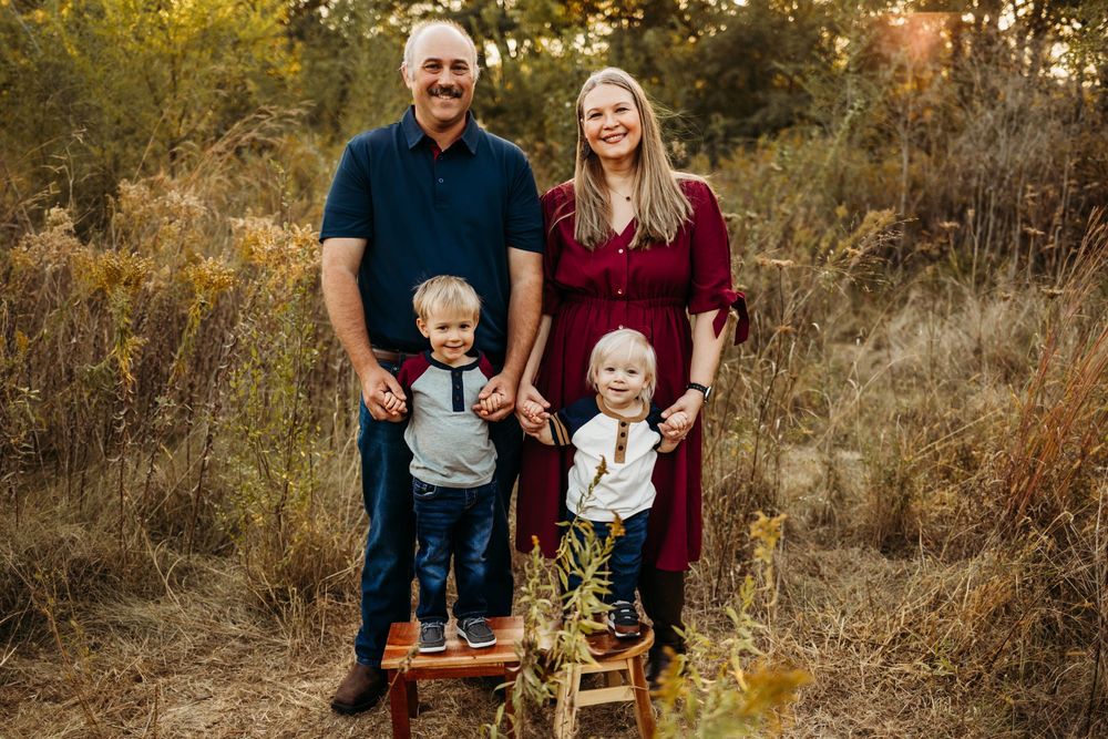 Family wearing burgundy and navy outfits poses together in autumn foliage during outdoor photo session.