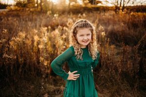 A child in an emerald green dress twirls playfully in golden autumn sunlight.