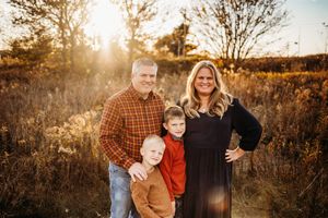 Candid family photo shoot in a rustic field with warm sunlight filtering through autumn foliage.