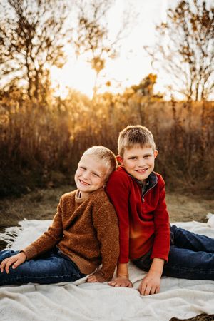 Children laying on white blanket during golden hour outdoor photoshoot.