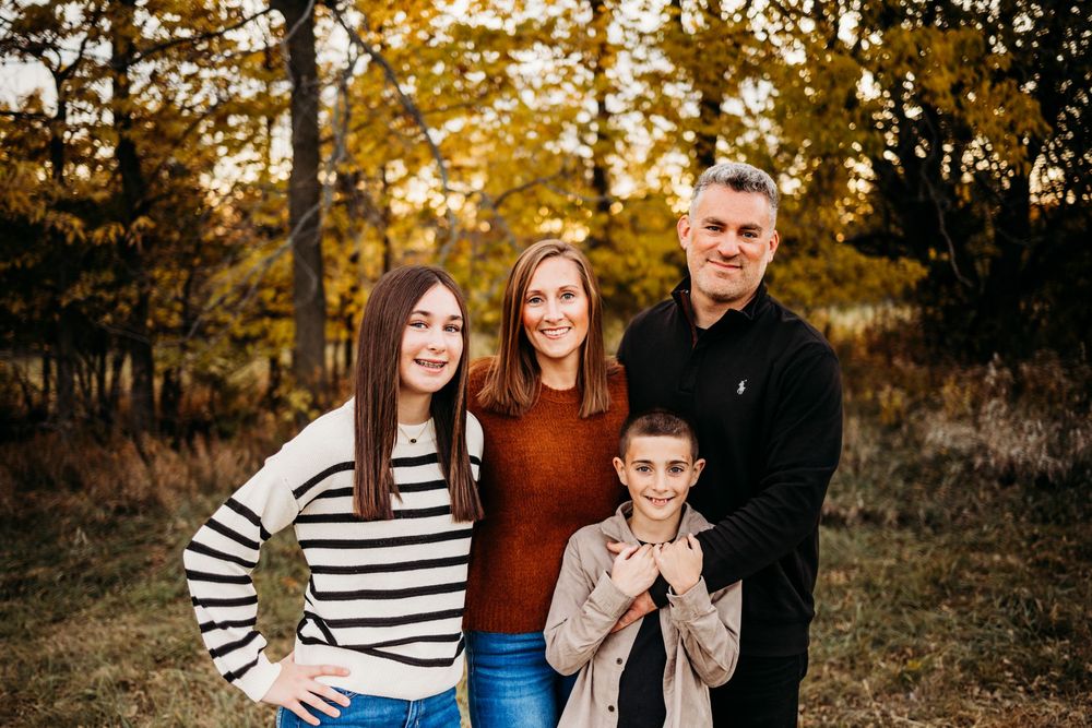 A family poses together in an autumn forest setting wearing coordinated outfits of stripes and warm colors.