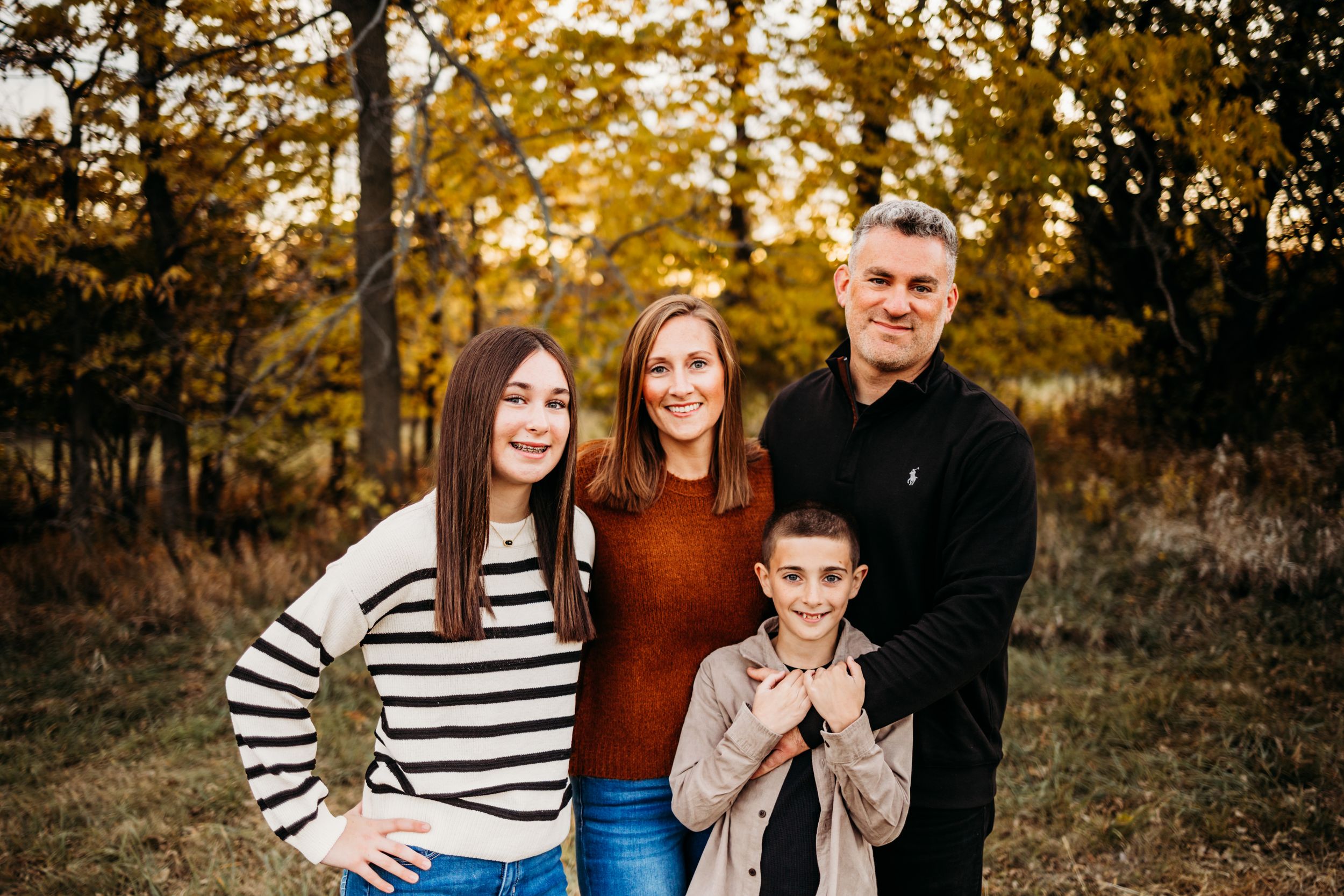 A family poses together in an autumn forest setting wearing coordinated outfits of stripes and warm colors.