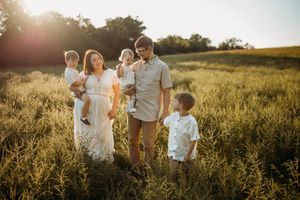 Family silhouettes walking together in a sunlit meadow during sunset.