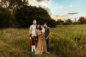 A family enjoys a sunset photoshoot in a serene meadow with dramatic evening sky.