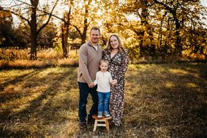 Family portrait session in a rustic field with warm golden sunlight filtering through autumn trees.