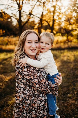 A joyful embrace captured during golden hour in an autumn setting with warm sunlight filtering through trees.