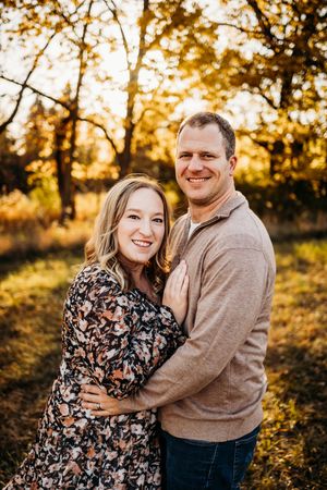 Couple embraces during golden hour photoshoot in a scenic autumn setting.
