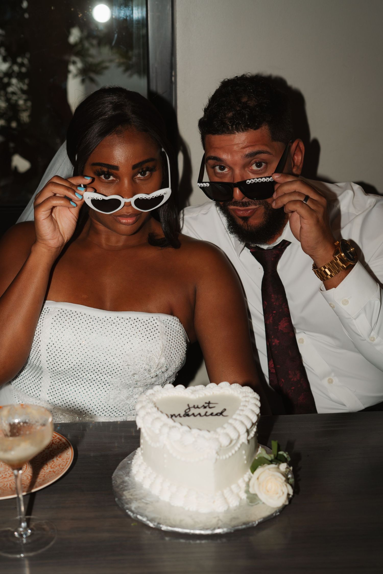 Playful scene of people wearing sunglasses while sharing a white cake at a table.