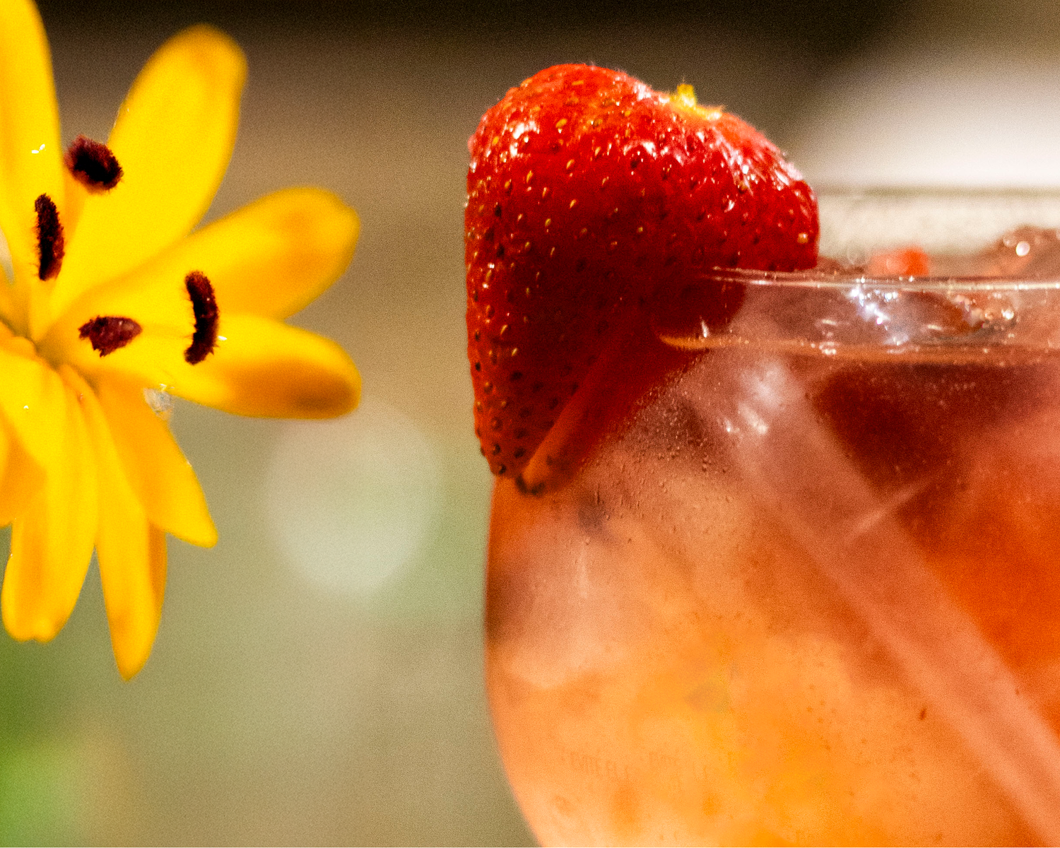 A refreshing strawberry cocktail garnished with a fresh strawberry slice and yellow flower on the rim.