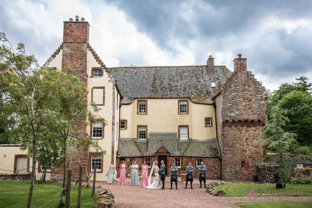 A row of historic stone buildings with gardens and enclosed courtyards seen under a dramatic cloudy sky.