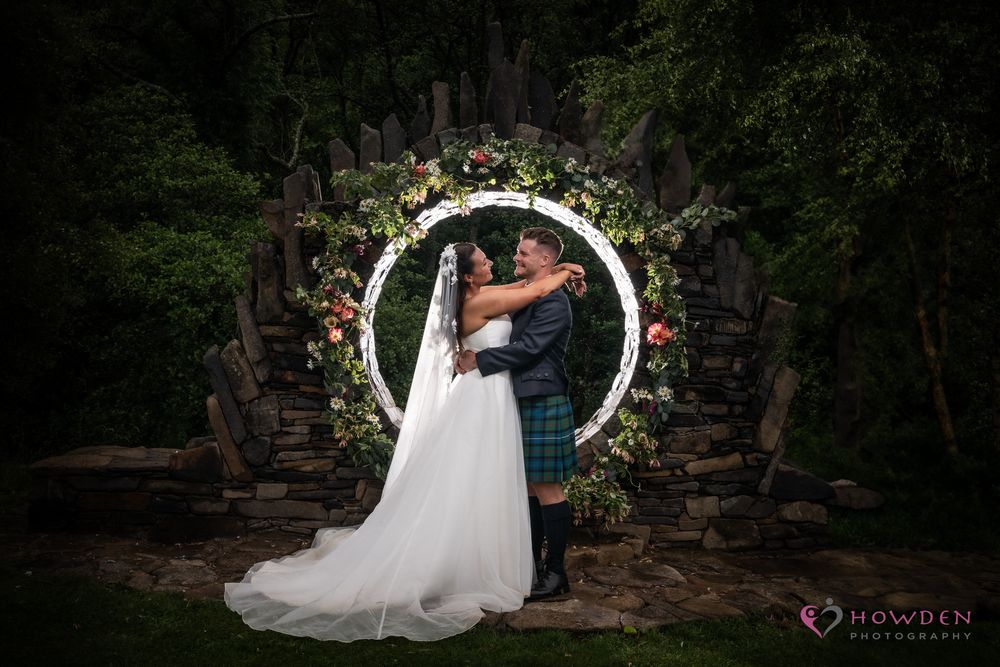 A romantic scene of a couple in wedding attire posing in a lush forest garden setting.