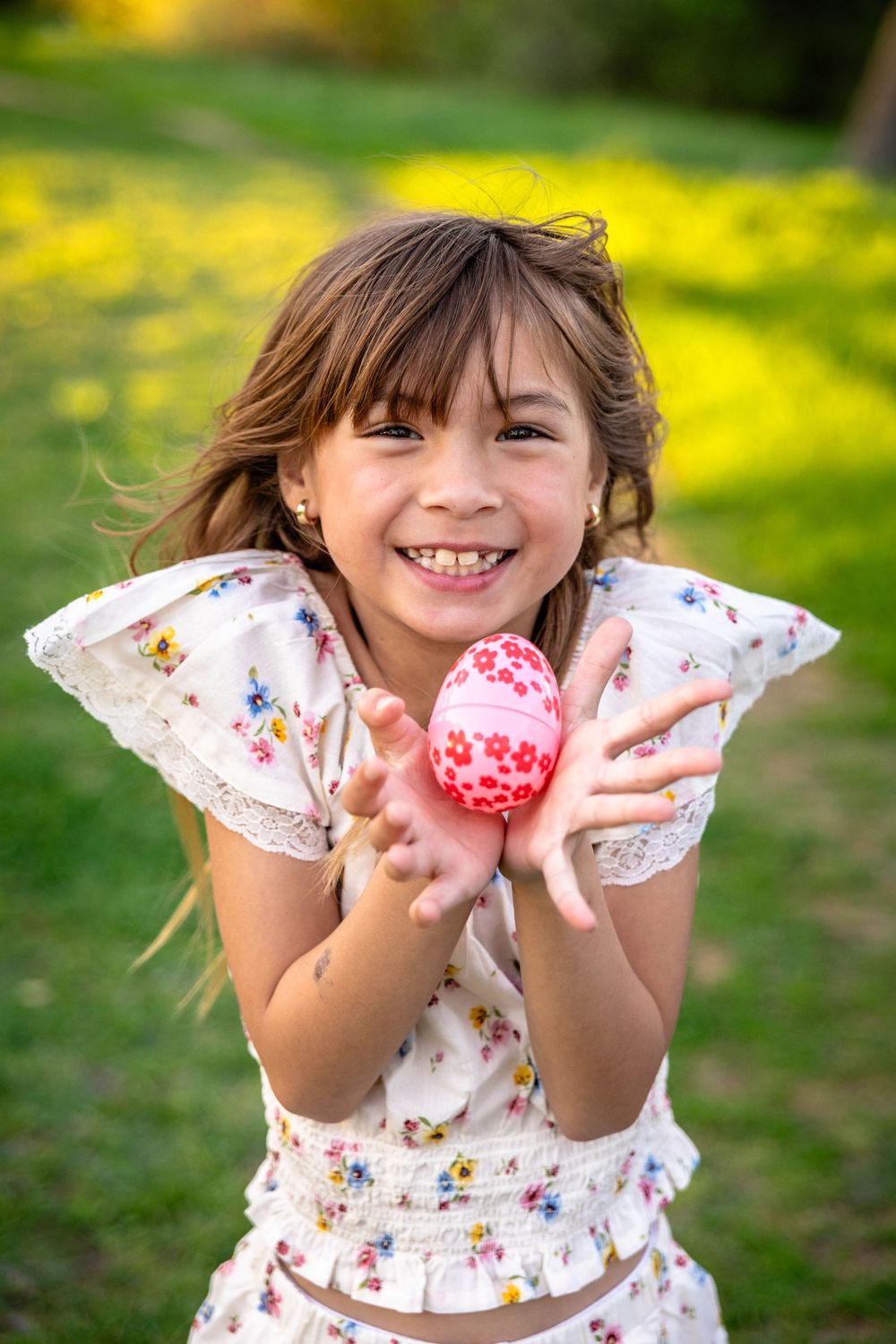 A young girl poses in green grass with a decorated Easter egg.