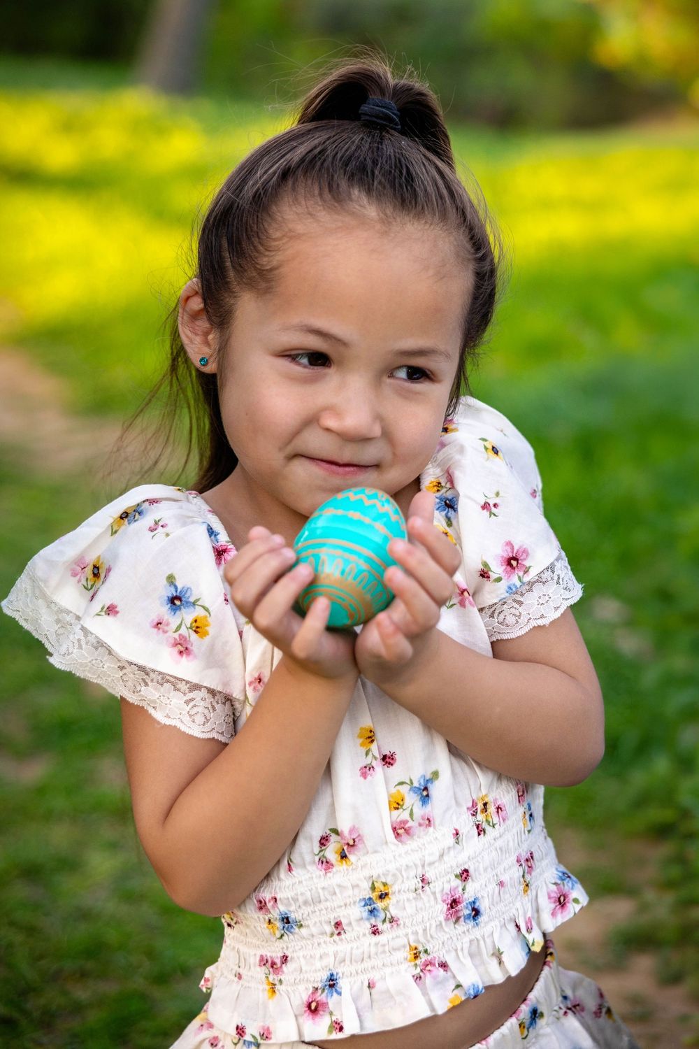 A young girl poses in green grass with a decorated Easter egg.