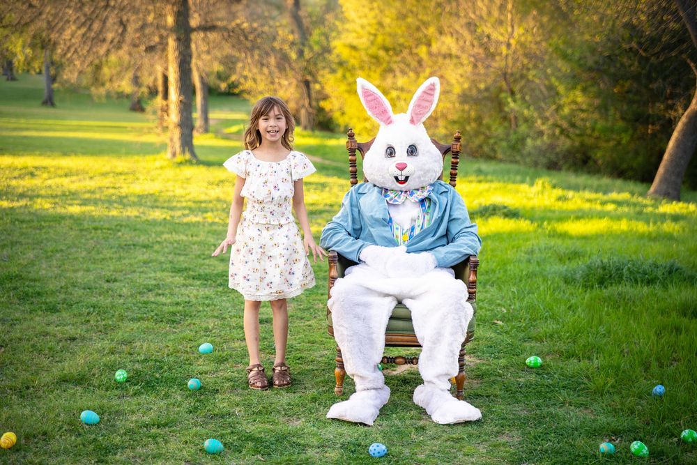 A young girl poses in a beautiful green field with the Easter Bunny in an antique chair.
