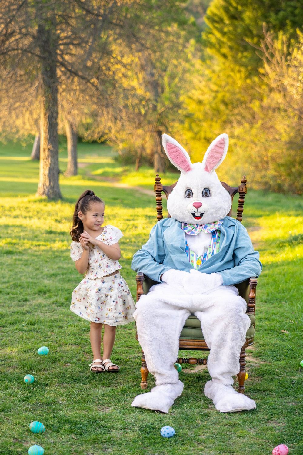 A young girl poses in a beautiful green field with the Easter Bunny in an antique chair.