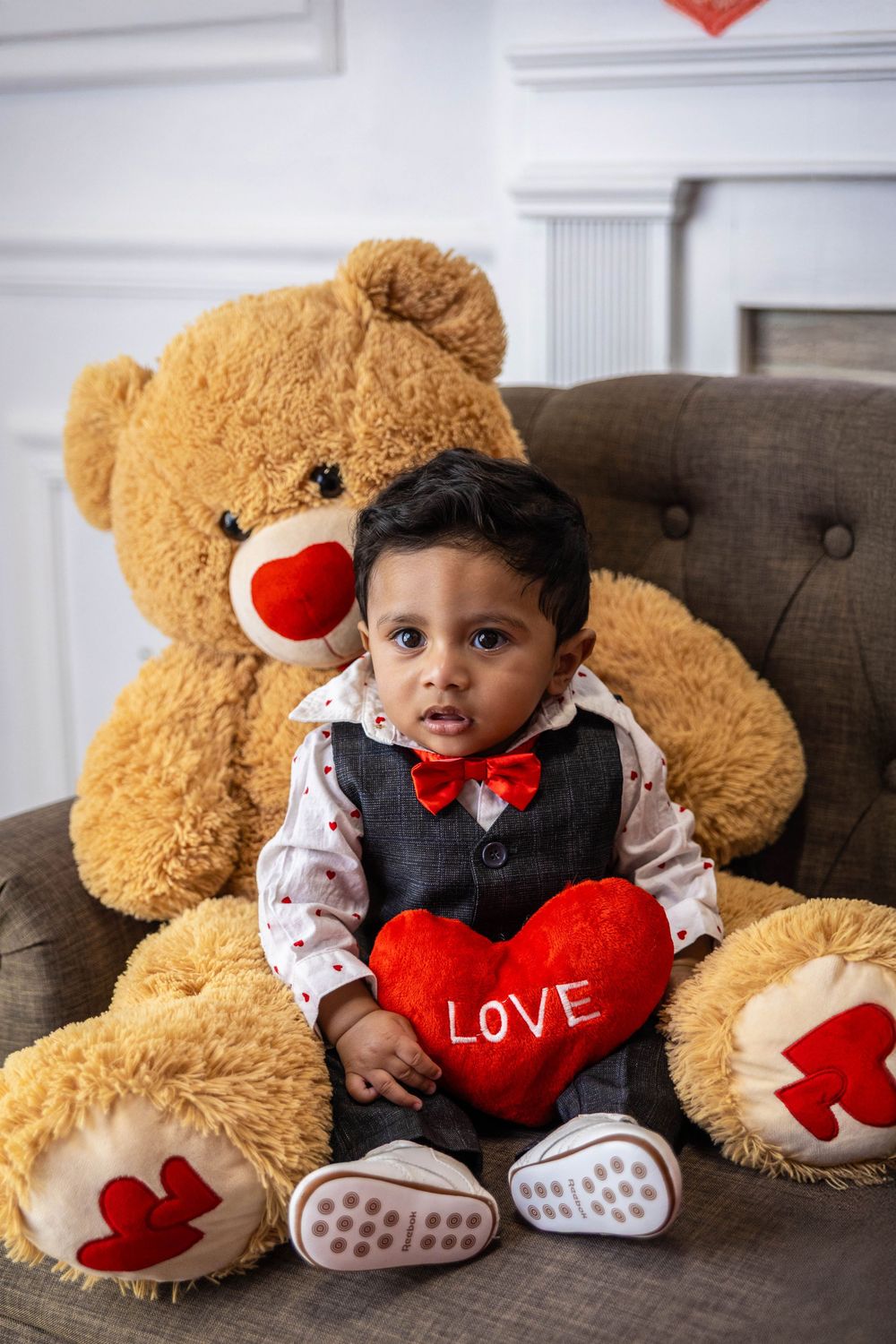A little boy poses with a bear on a couch.