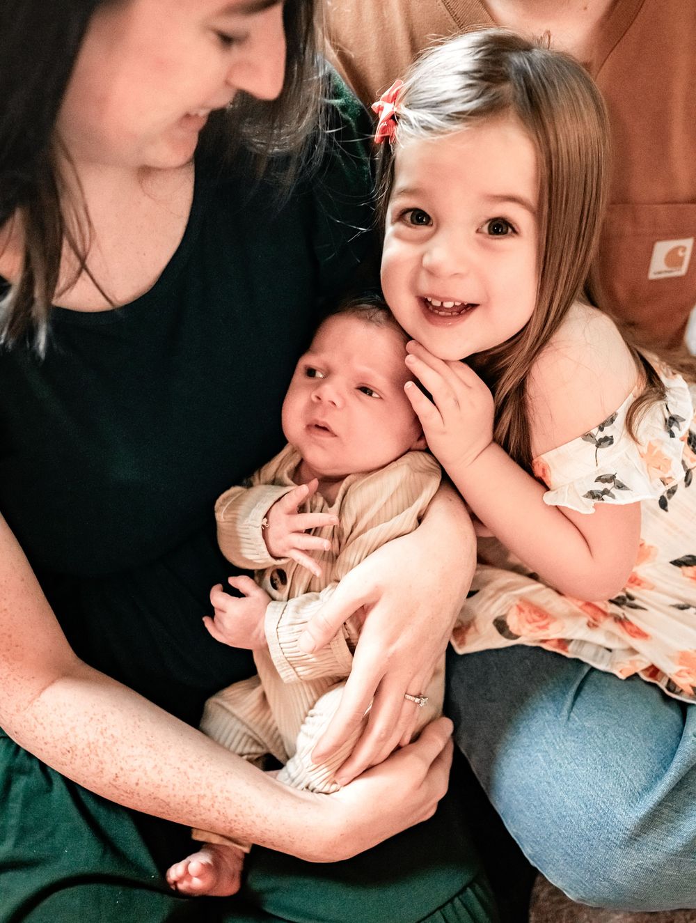 A heartwarming family moment captured as a toddler and parent cuddle with a newborn baby.