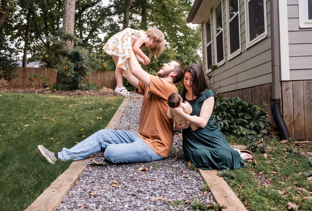 Playful family moment captured outdoors on a patterned rug near their home.
