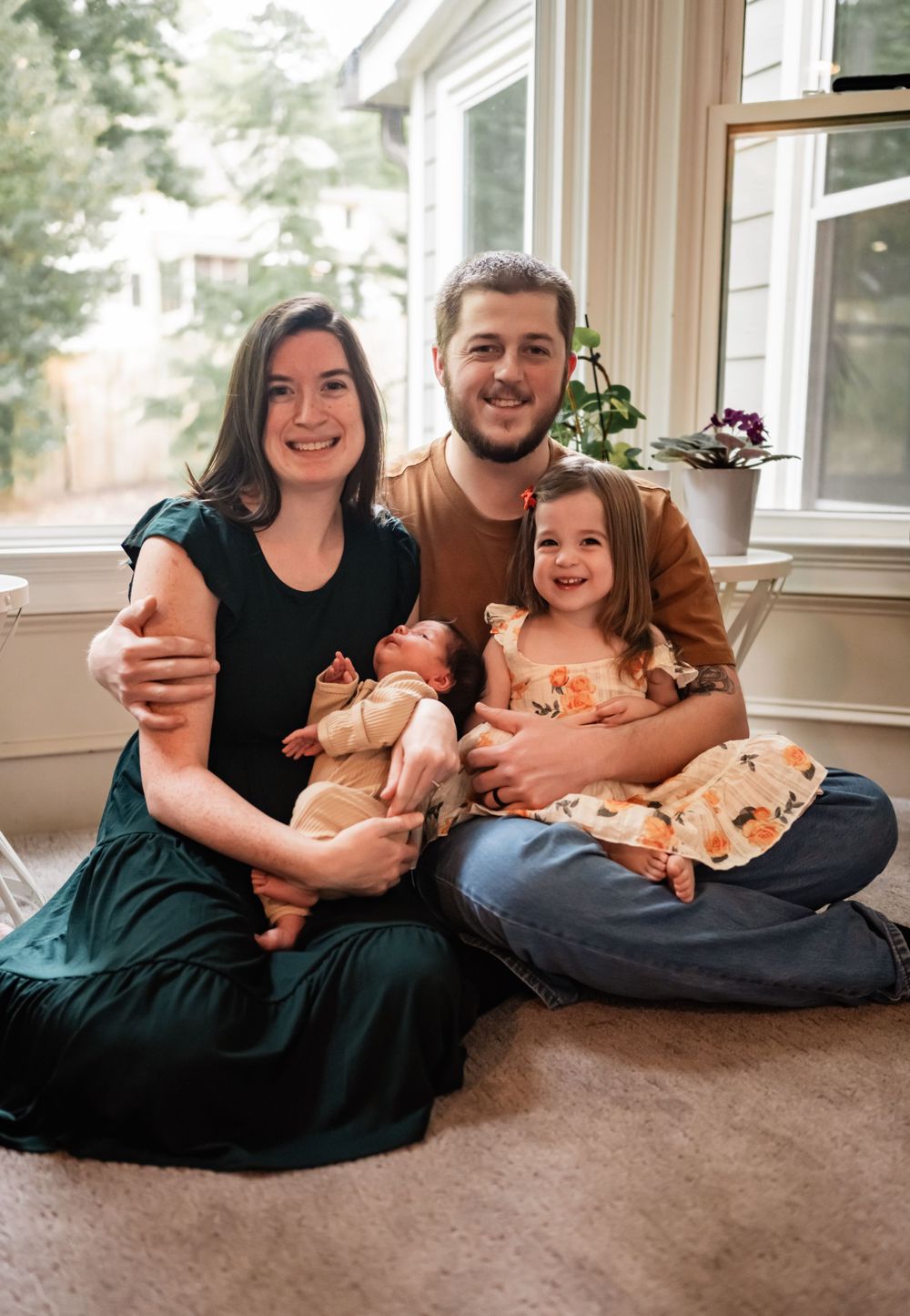 Family portrait in a sunlit room with houseplants showing a cozy gathering on carpet.