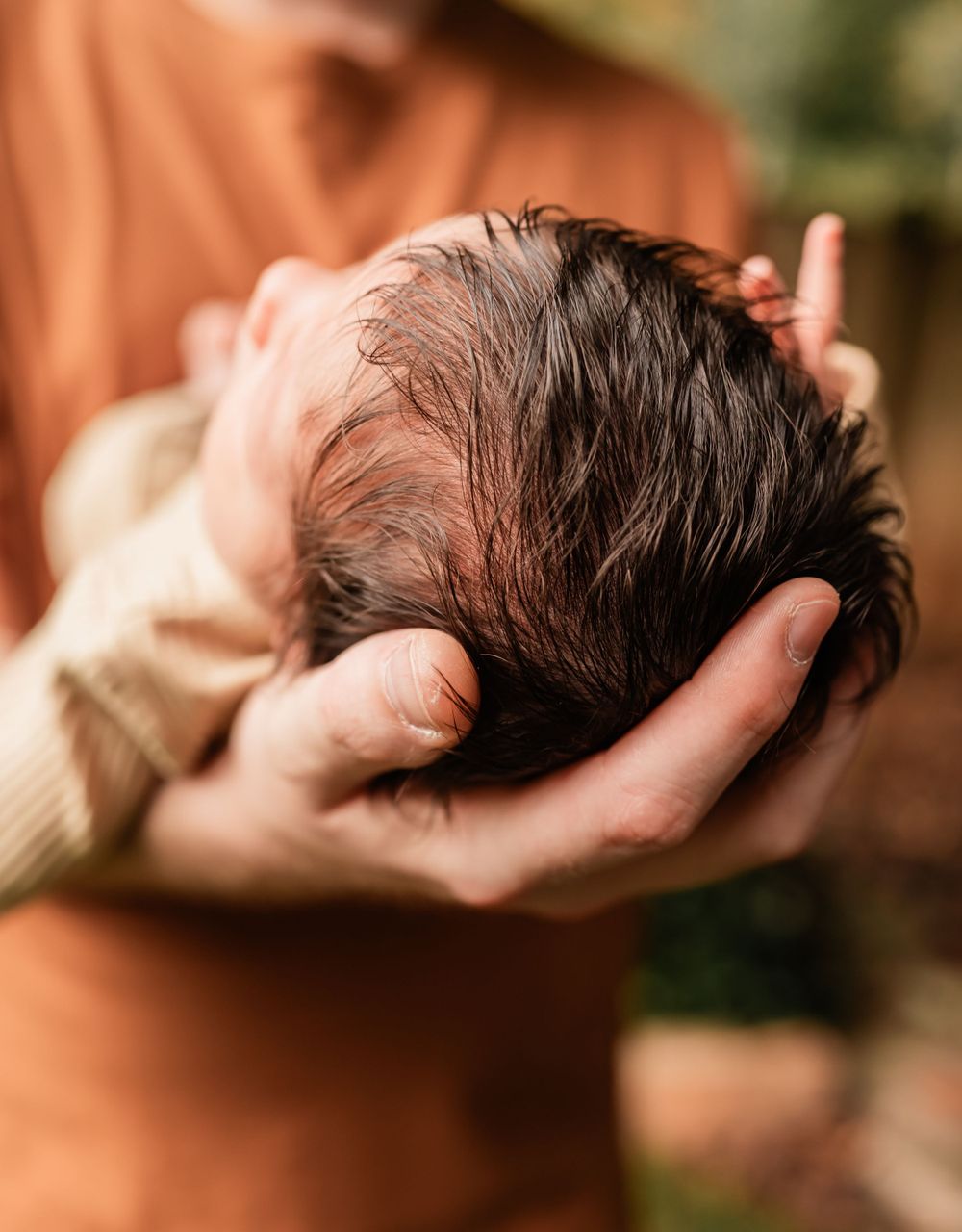 Close-up shot of a baby's dark hair being gently cradled.