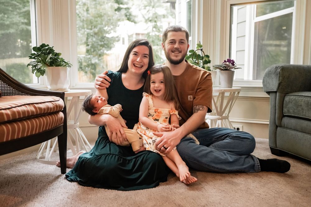 Casual family photo session in a bright sunroom with large windows.