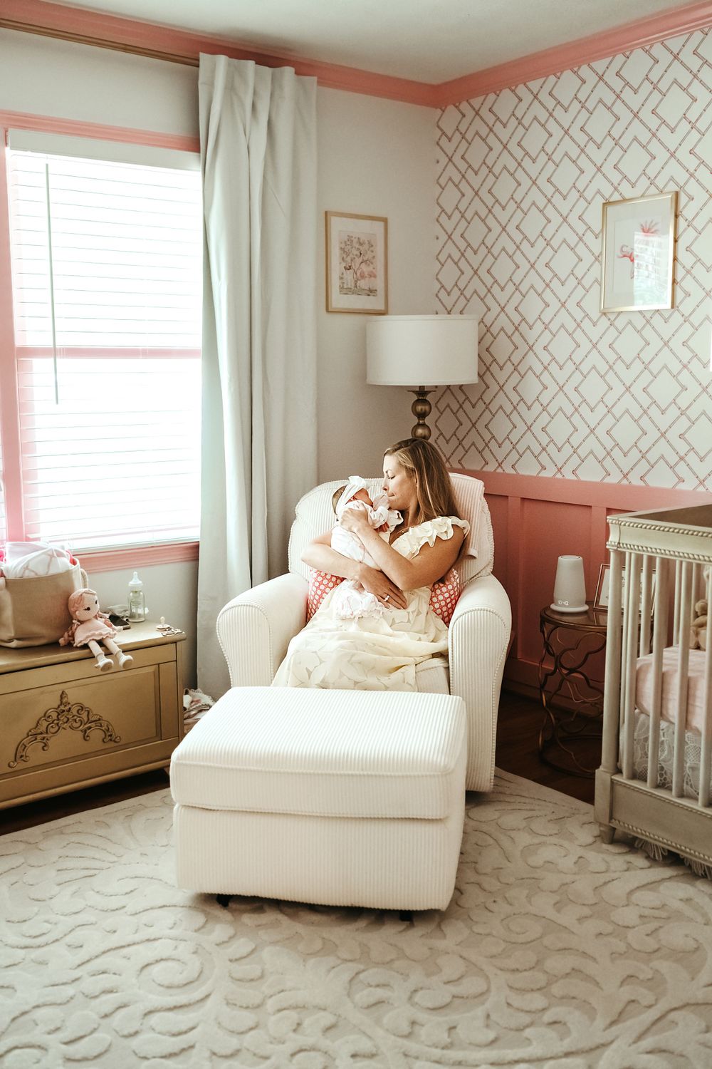 Cozy nursery with white glider chair, geometric wallpaper, and pink accents features modern design elements.