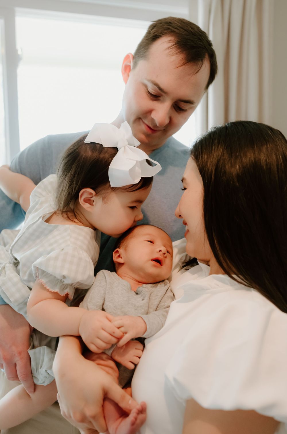 Loving family shares intimate moment together while holding newborn baby in white onesie at home.