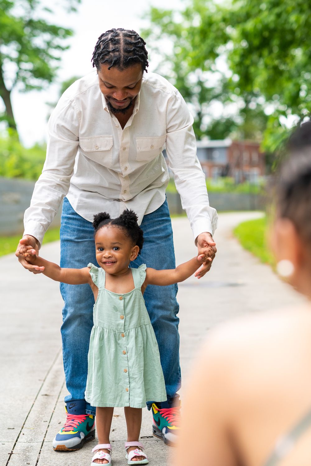 A father holds the hands of his daughter as she walks towards her mother.