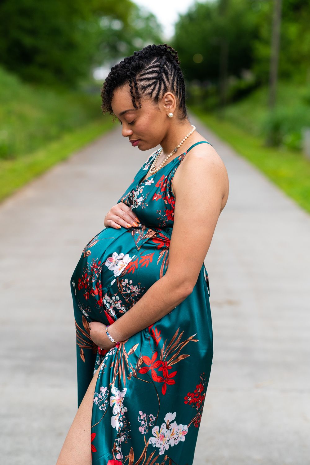 A woman in a green dress looks down at her pregnant belly.
