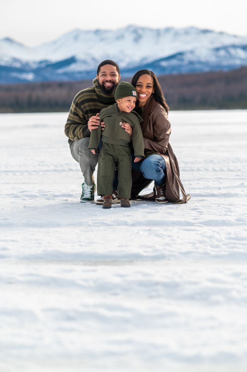 A family takes the portrait outside in the icy snow with mountains in the background.