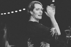 Black and white photo of an elegant woman in a floral dress gesturing gracefully at a formal evening event.