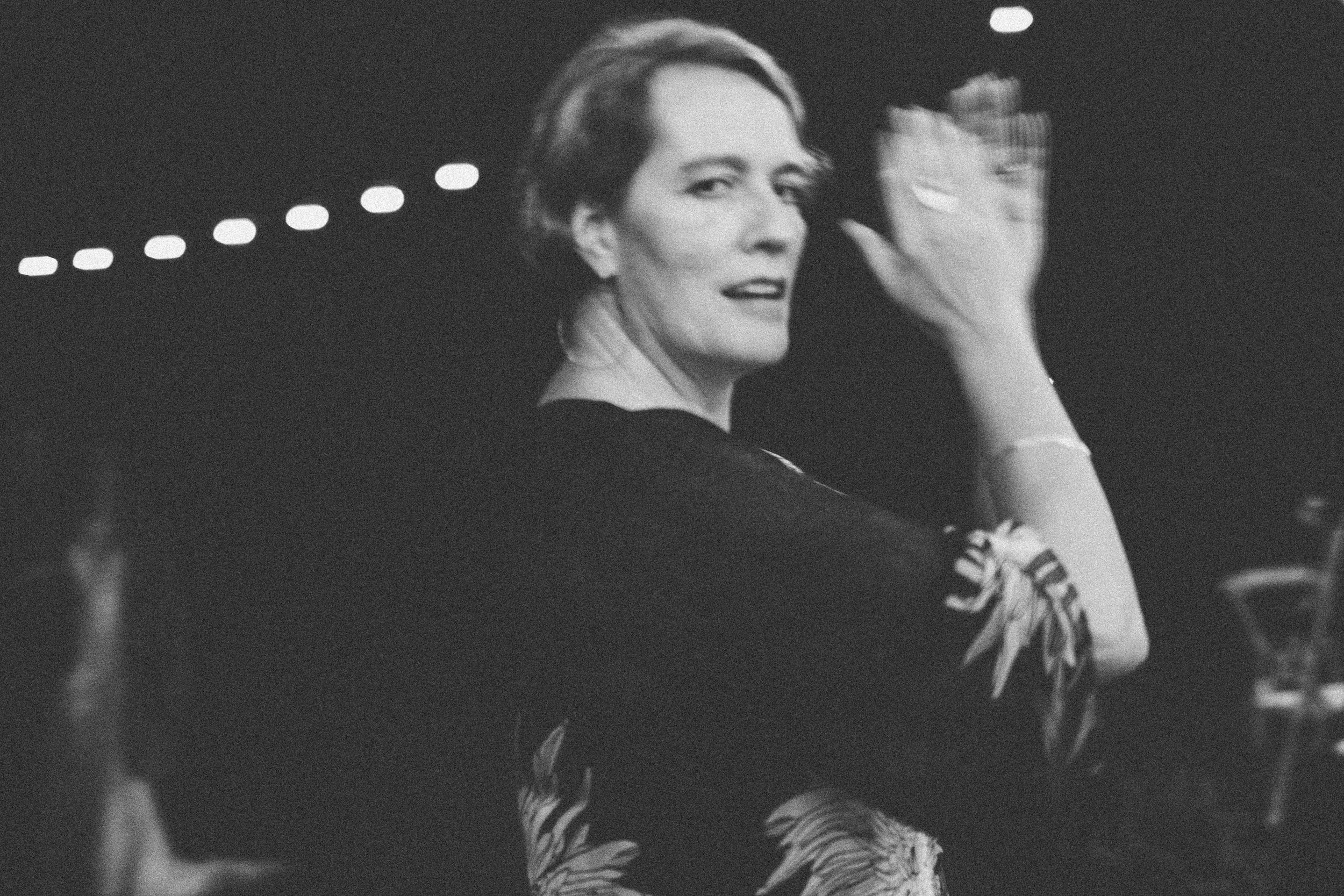 Black and white photo of an elegant woman in a floral dress gesturing gracefully at a formal evening event.