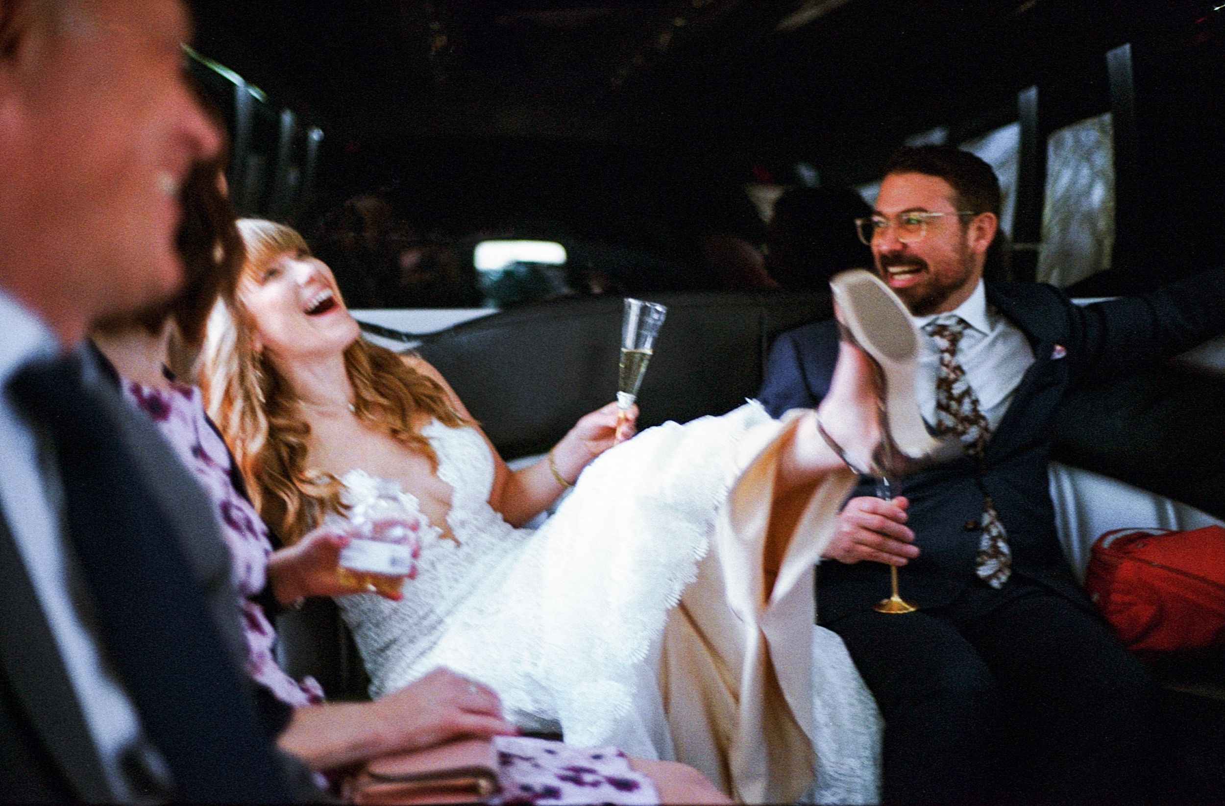 Bride and groom laughing in a limousine, holding champagne glasses, celebrating their wedding day.