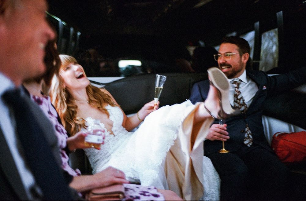 Bride and groom laughing in a limousine, holding champagne glasses, celebrating their wedding day.