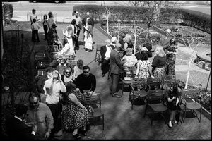 Aerial black and white photo of a crowd gathered at outdoor tables and chairs at a social event.