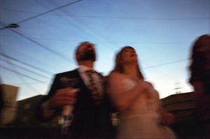 Motion-blurred color photo of a bride and groom walking together outdoors at dusk under power lines.