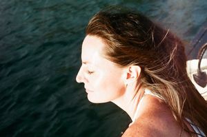 Woman with windswept hair relaxing on a boat with dark green ocean water in the background.