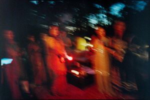 Blurred color photo of people gathered outdoors at night with glowing warm orange light.