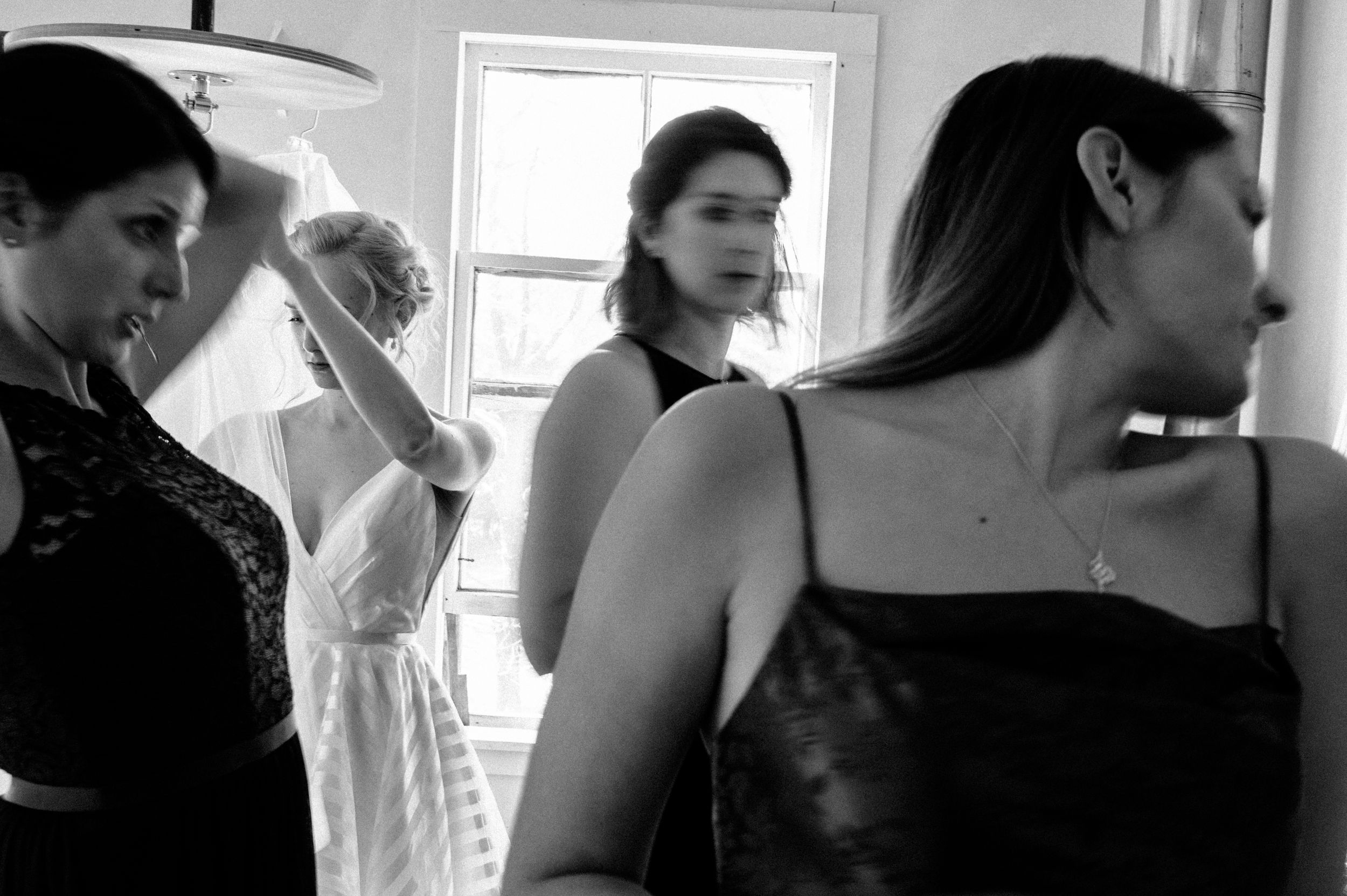 Black and white photo of women in formal attire preparing for a wedding ceremony indoors.