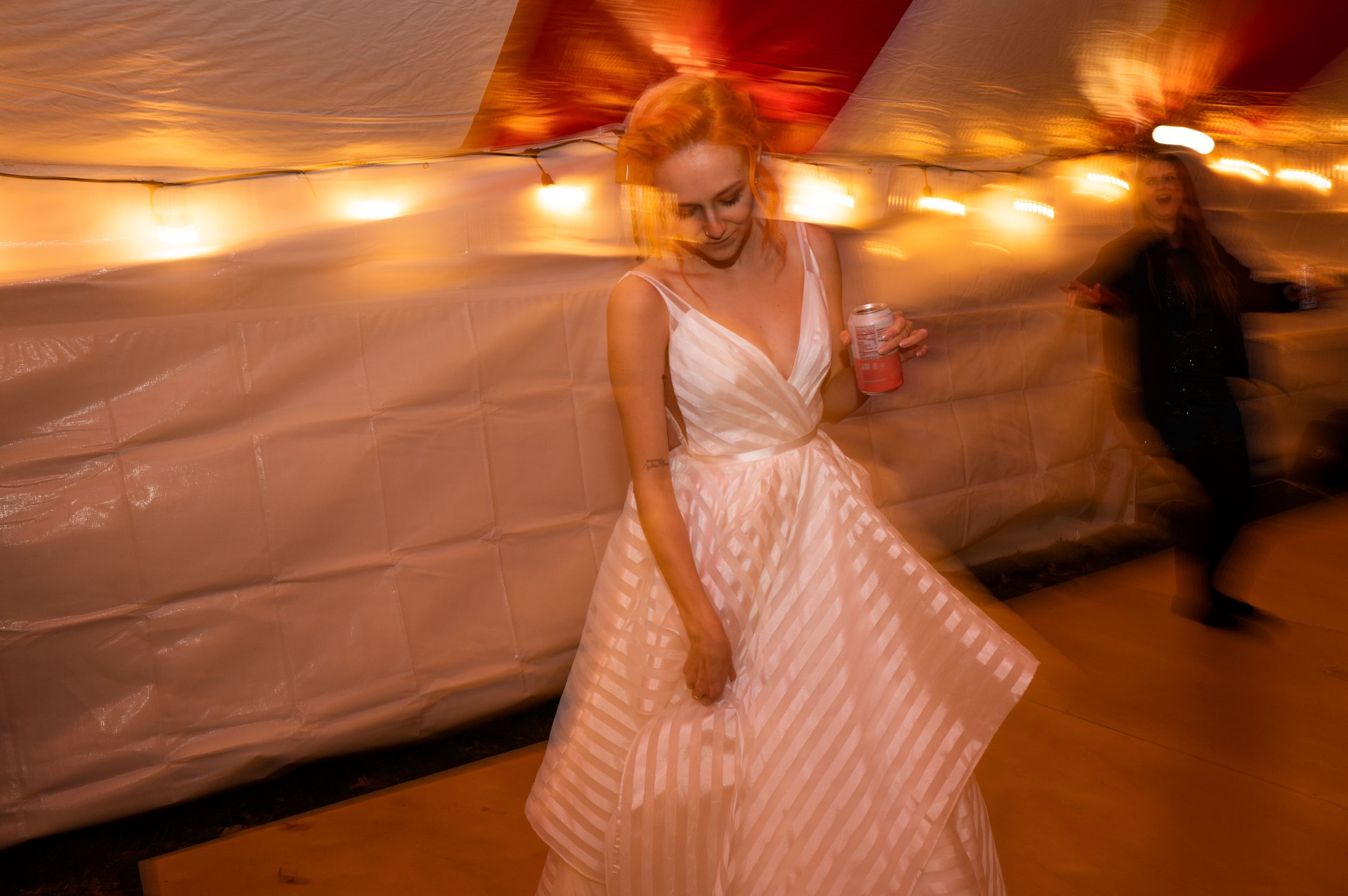 Woman in striped ball gown twirling at a festive event with warm string lights in a decorated tent.