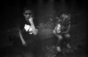 Black and white photo of two young children standing on wet pavement at night.