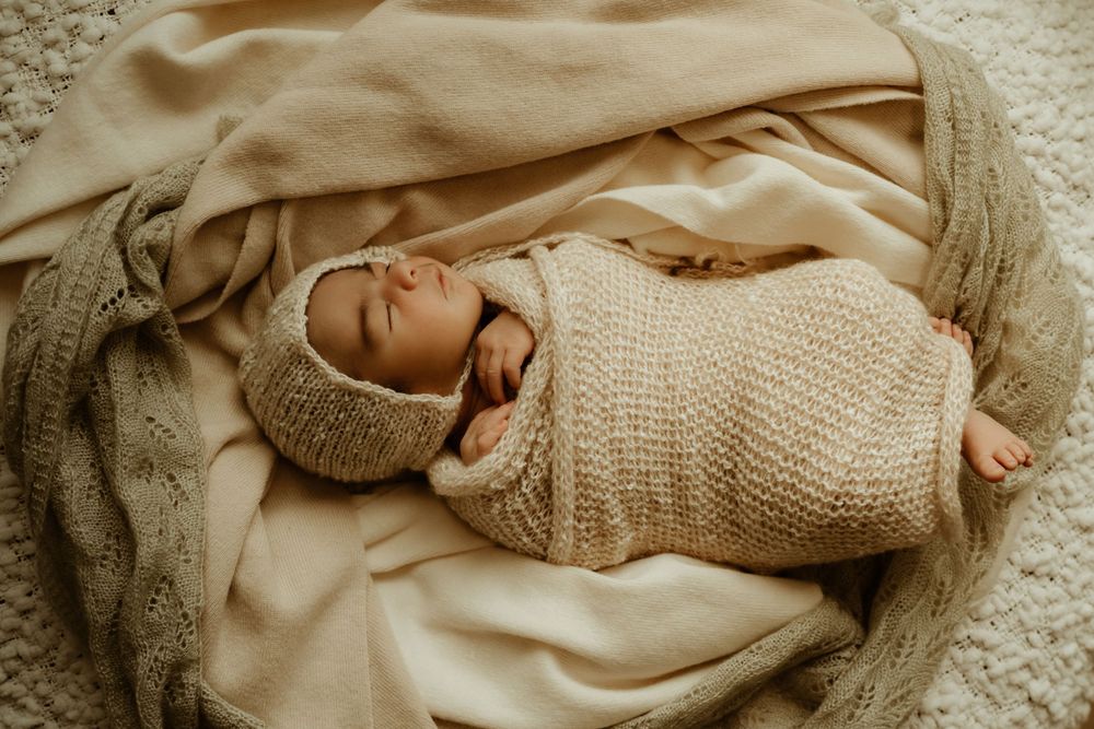 Newborn baby swaddled in a neutral knitted blankets with a matching bonnet