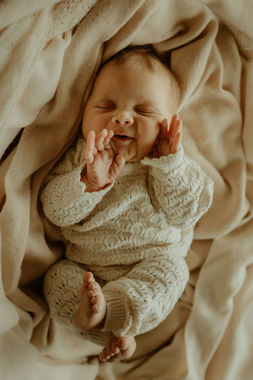 A sleeping baby wearing a white knit sweater lies peacefully on cream-colored bedding in a series of connected photos.