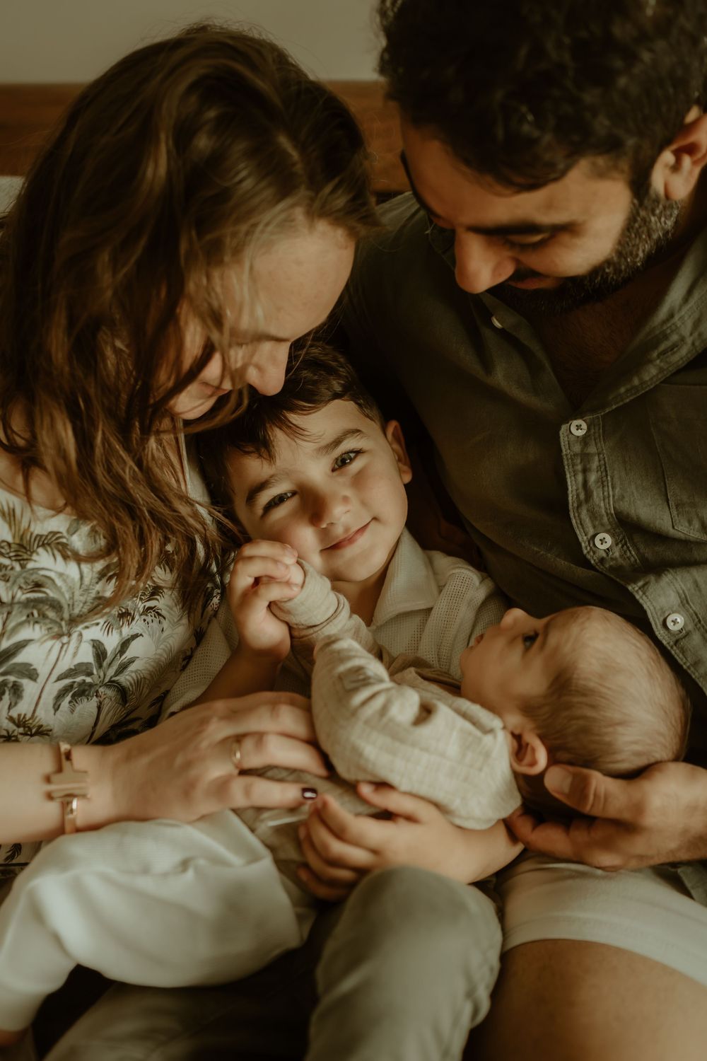 Intimate family moment showing parents snuggling with their newborn baby in warm, moody lighting.