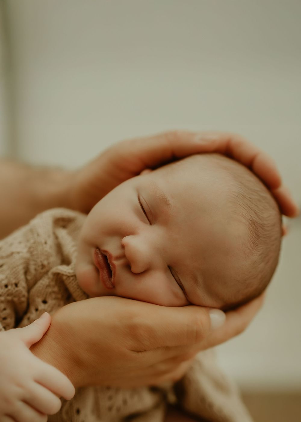 Newborn baby sleeping peacefully in gentle hands, wrapped in a soft knit blanket.