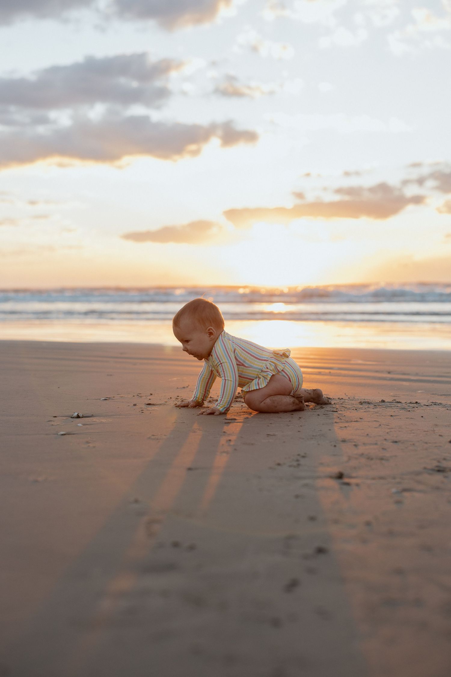Baby crawls on beach sand during golden sunset.