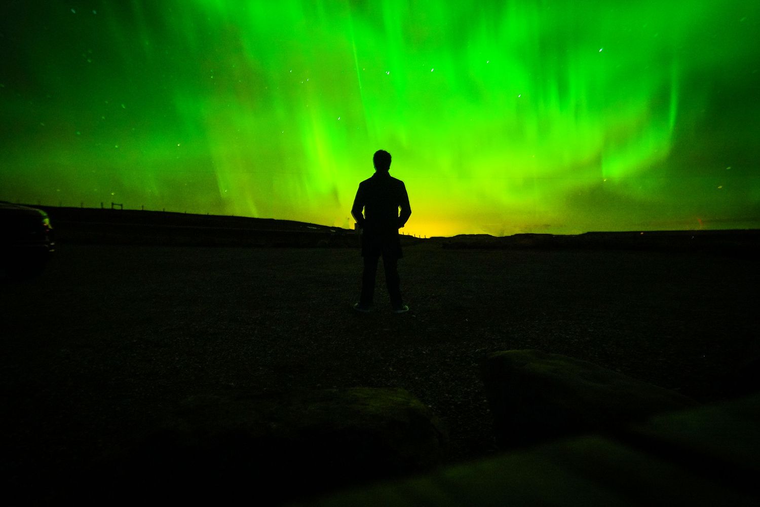 Silhouette against vibrant green northern lights in the night sky.